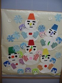 折紙による壁面装飾。雪がふるなか、手袋にバケツの帽子、野菜で作った鼻の雪だるまが楽しそうに並んでいます。