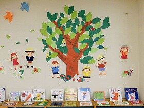 画像:たくさんの葉っぱをつけた大きな木と、その周りで遊ぶ子どもたちの絵の切り紙装飾。