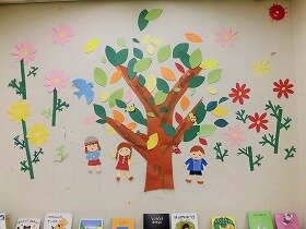 画像:葉っぱが色づき始めた大きな木と、その周りにたくさんのコスモスが咲いている壁面飾り。