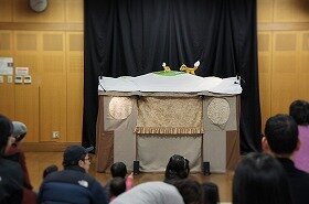 画像:人形劇団あっぷうが演じる紙芝居と人形劇に、それぞれお客さんたちが見入っている写真です。