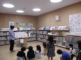 画像:大型絵本のよみきかせをしている職員と、きいている親子。