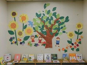 画像:大きな木、ひまわりとあさがお、その周りで遊ぶ子どもたちの切り紙装飾