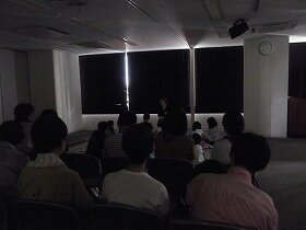 画像:暗い部屋でおはなしをする演者ときいている親子