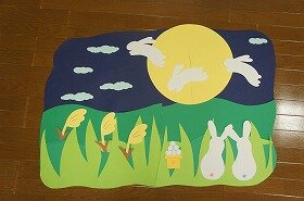 画像:月の中で飛び跳ねるうさぎたちを、地上にいるうさぎたちが寄り添いあって見ている壁面装飾です。