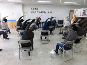 画像：椅子に座って片腕をのばすストレッチを行う参加者たち
