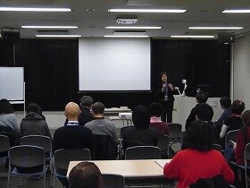 画像：上映前の会場の様子。司会者の挨拶に耳を傾ける参加者の方々。