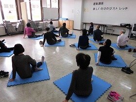 画像：マットの上で上体をひねるストレッチを行う参加者たち