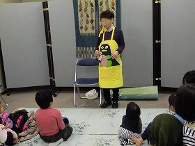 画像：黄色いエプロンに緑のかいじゅうのエプロンシアターの様子。