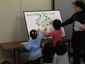 画像：パネルシアターで、子どもたちが枝にブタの実を付けています。