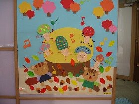 画像：落ち葉や木の実の上でキノコとリスが踊っている。