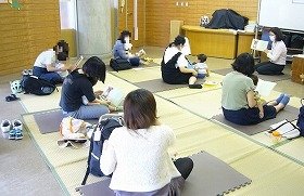 画像：講師の読み上げを手本に、ひざの上のお子さんといっしょに絵本を読んでいる様子。