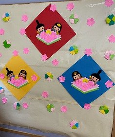 画像：桃の花に囲まれたおひなさまとおだいりさまが、ひし餅を食べようとしている。