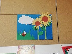 画像：青い空と白い雲の下に、大きなひまわりが咲いている。