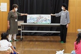 画像：大型絵本「きょだいなきょだいな」の読み聞かせをしている様子。