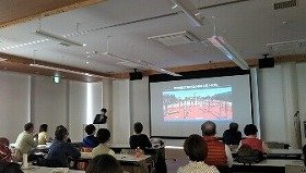 画像：健都レールサイド公園の健康増進広場の写真をスライドに映し、設置されている健康遊具の説明を始めるところです。