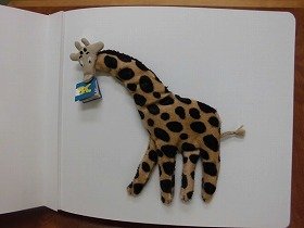 画像：さわる絵本の1頁。本を口にくわえたきりん。