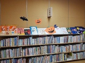 画像：色画用紙で作られた壁面装飾3点。ススキの野原でトンボと遊ぶ子供たち、満月、コウモリとおばけとジャック・オ・ランタン。