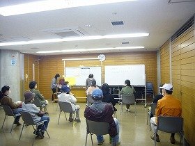 画像：集会室で講師の話を聞く参加者。