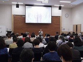 多くの参加者と白雪姫について話す講師の正置友子さんの画像。スクリーンには白雪姫の絵本が映し出されている。