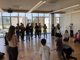 画像：A4サイズの大きなカルタを囲んで競技を行う様子