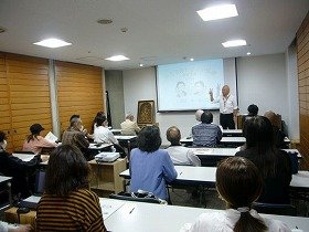 写真：スクリーンの前に立って話をする講師と話を聞く参加者たちの画像