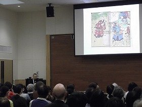 画像：多くの参加者と講師。スクリーンには昔の絵本が映し出されている。