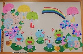 写真：楽しそうに歌うカエルたち、雨傘、あじさい、かたつむり、虹。6月の壁面装飾です。