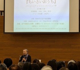 「ちいさいおうち」について話す講師の正置友子さんの画像。スクリーンには講座のタイトルが映し出されている。