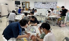 写真1：講師に教わりながら、紙コップけん玉を作っている参加者。