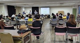 画像2：スクリーンを使って説明をする講師と話を聞く参加者