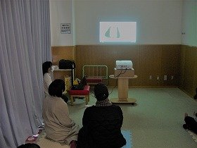 写真1：マルチメディアデイジー「おにぎり おむすび」を上映し、リズミカルな読み上げに体をゆらしている参加者たち。