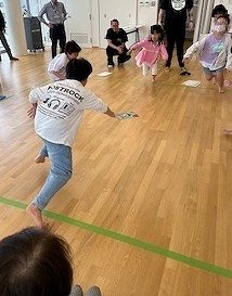 写真2：A4サイズの大きなカルタを囲み、読まれた札を一斉に取りに行く様子