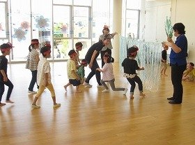 写真3：『スイミー』の物語を体感できる運動遊びで、クラゲを模した障がい物を子供たちが潜り抜けていく様子。