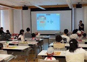 健康医療情報講座「親子で学ぼう「食育」と「健康」」で前方のスクリーンに映されたスライドを見ながら講師の話を聞いている参加者の様子の画像