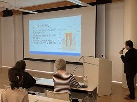 写真1：「放置すると危険！歯周病」の講座で、講師が歯周組織の構造について説明し、参加者が聞いている様子
