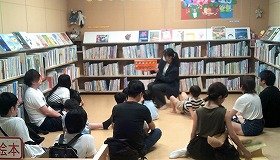 図書館実習生が大勢の親子に絵本『しろくまちゃんのほっとけーき』を読んでいるところの画像