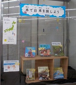 中央図書館1階ガラスケース内に東北や東京、沖縄など日本各地が舞台の本を展示している様子の画像