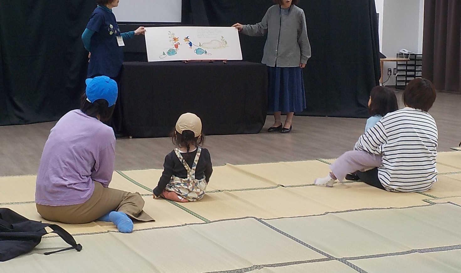 写真１：大型絵本「ぐりとぐらのえんそく」の読み聞かせを聞いている参加者