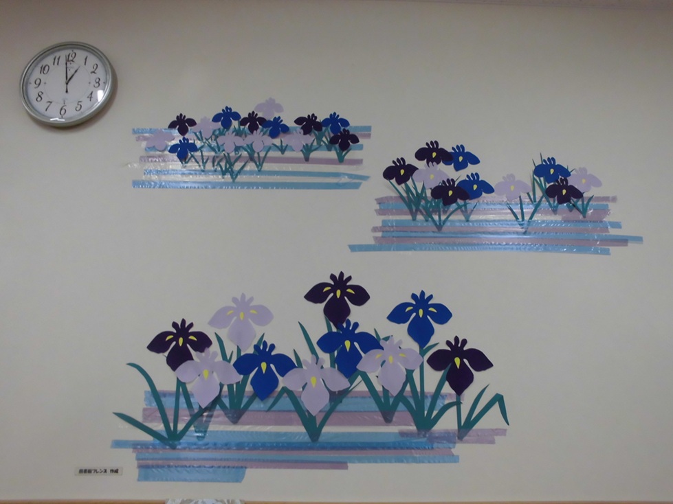 写真壁面に紫や青の切り絵の菖蒲が群生するように大中小で飾られています。