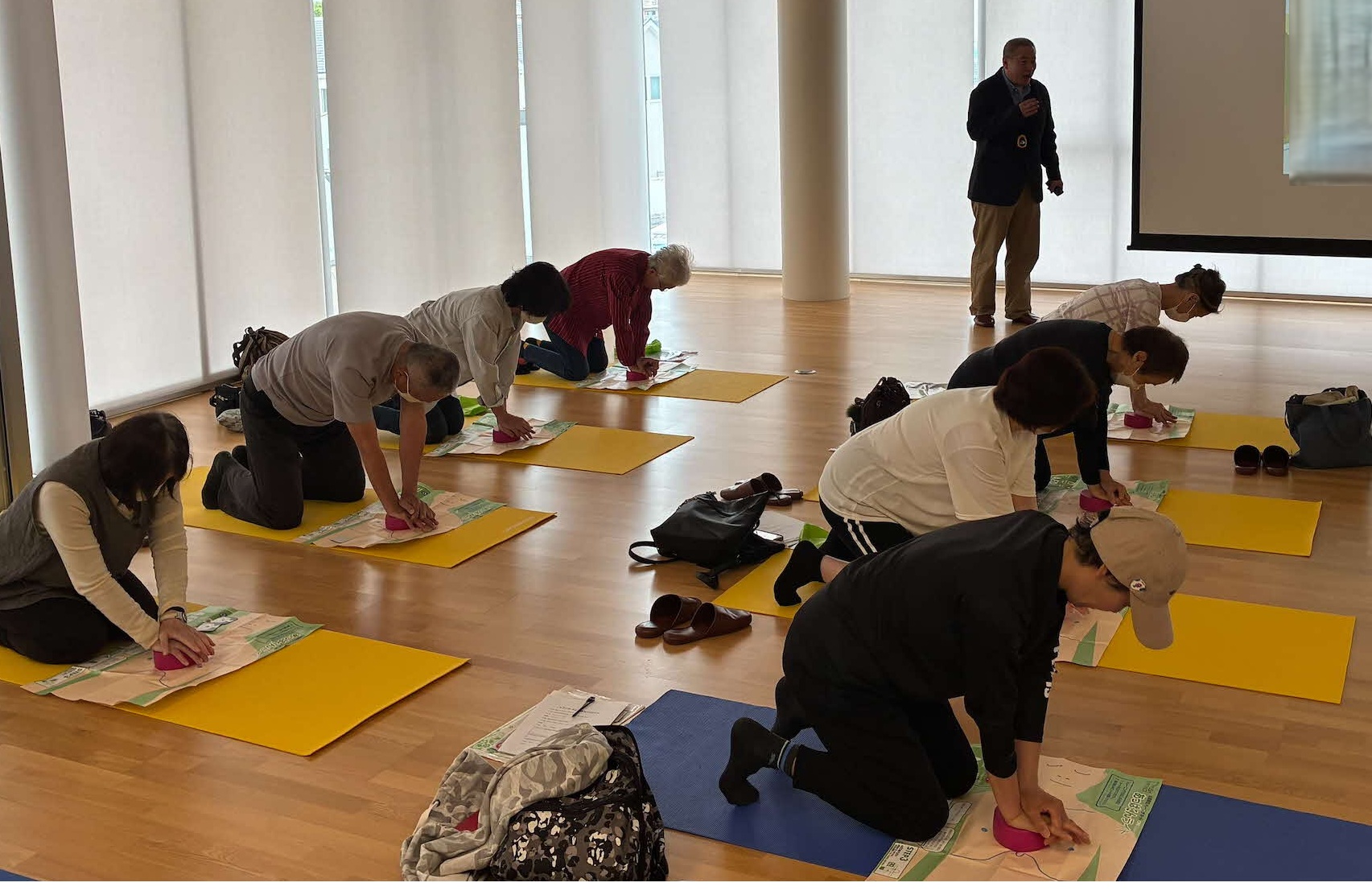 写真健康医療情報講座「キミもともだちをすくおう！PUSHコース受講会」で講師の説明を聞きながら胸骨圧迫の訓練をしている参加者の様子
