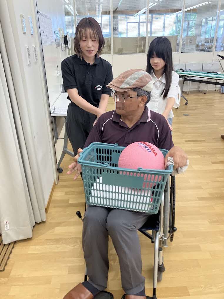 健康医療情報講座「病気やけがで動きにくい人のからだのはなし」で講師と共に車いすの体験をしている参加者の様子。