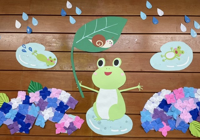 紫陽花が咲く雨の中、カエルは水たまりで泳ぎ、カタツムリはカエルが持つ葉の上でくつろぐ様子。