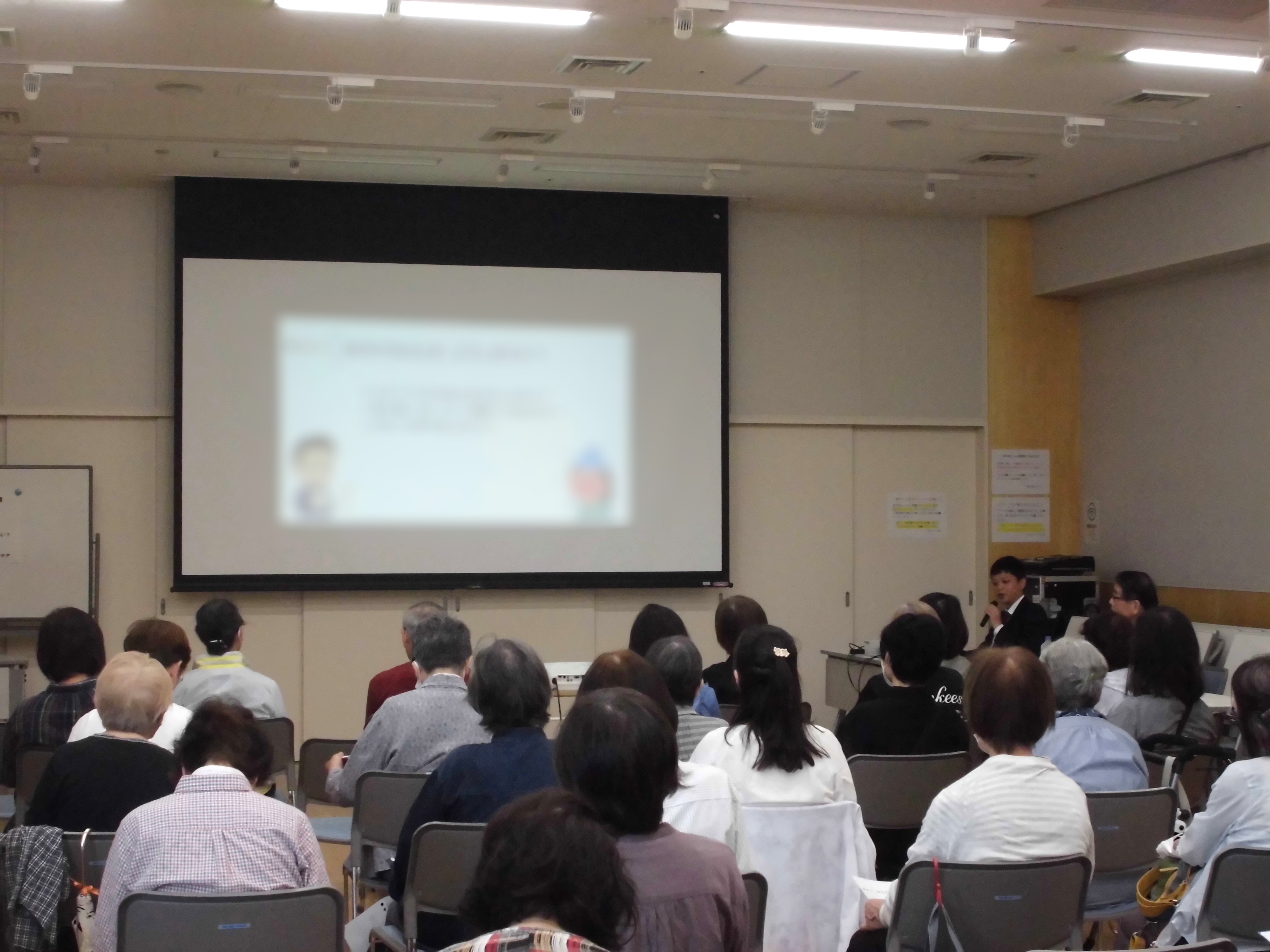 写真「この症状、病院に行くべき？様子見でいい？」の講演で講師のお話に耳を傾けながら前方のスクリーンを見ている参加者の様子。