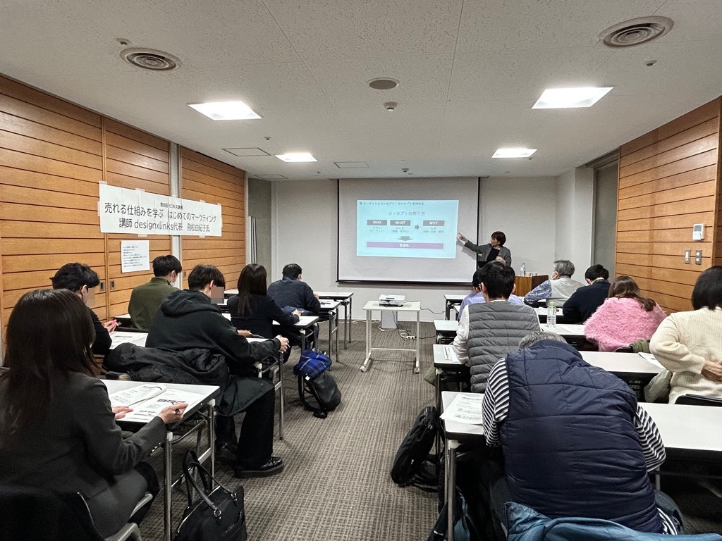 写真：スクリーンの資料を指す講師と講師の話を聞く参加者たち