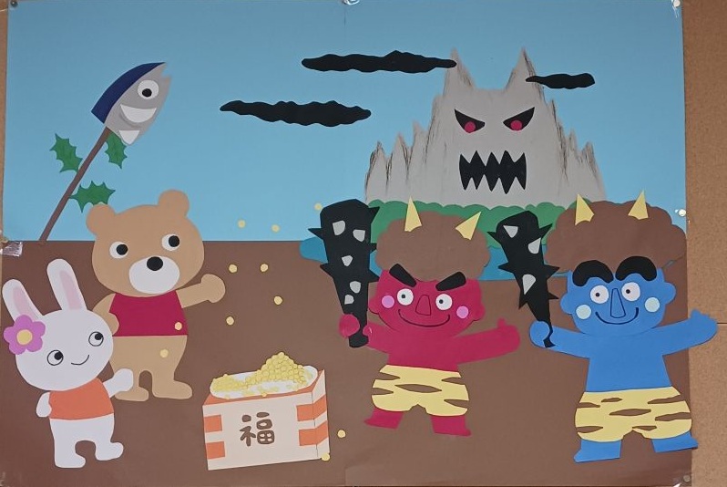 写真：画用紙と折り紙で作った節分の壁面飾りです。赤鬼と青鬼が棍棒を持って立っているところへ、うさぎとくまが豆まきしています。