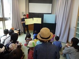 親子連れの参加者の前で女性が紙芝居を読んでいます