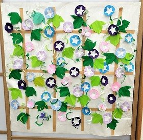 写真　格子状の柵に満開の朝顔の花が、たくさん咲いている。柵には朝顔のツルが絡みついている。