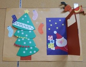 写真2：左側には画用紙でつくったもみの木があります。右側には、ドアをあけてプレゼントを持ったサンタクロースが入ってきた様子を画用紙と折り紙で表しています。