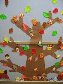 落ち葉が舞い散るなか、りすや栗・柿・どんぐりの妖精たちが木に登って遊んでいる壁面飾り。