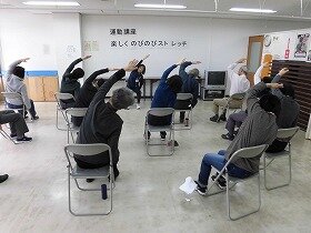 椅子に座って片腕をのばすストレッチを行う参加者たち